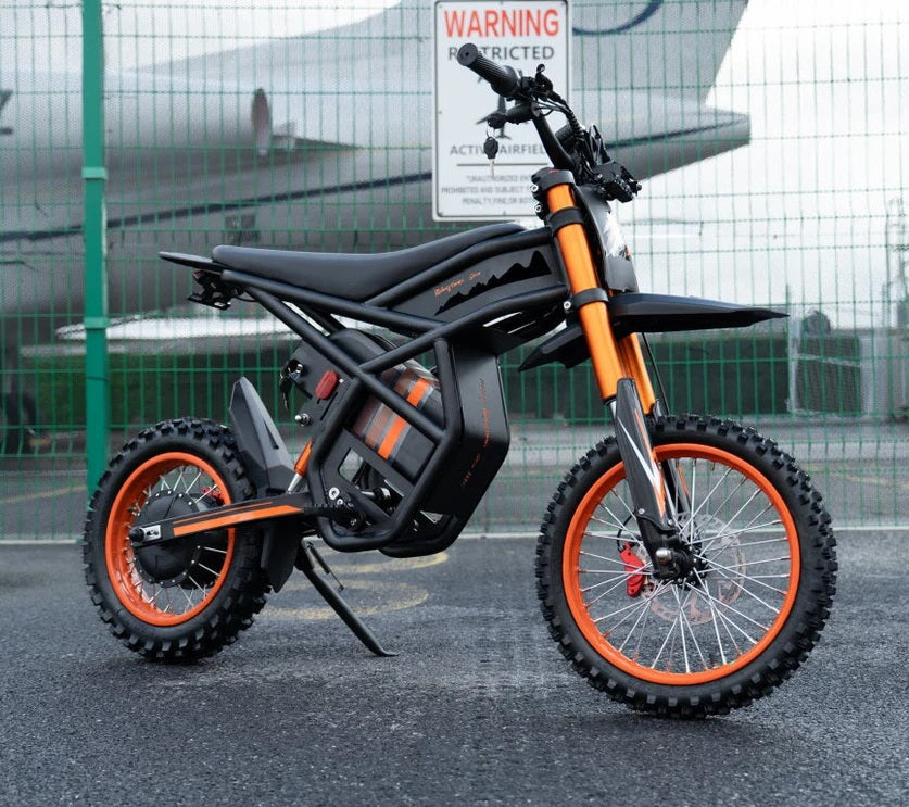 Riding Times GT54 off-road electric bike on a road with a fence and airplane in the background.