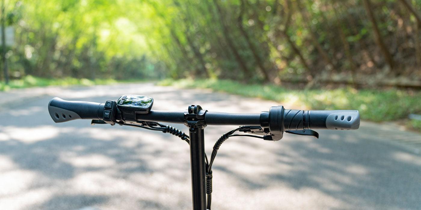 Electric bike handlebar with display, black grips, front view on a forest road