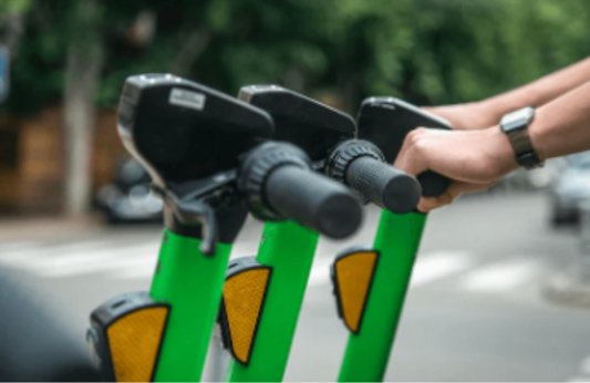 green electric scooters handlebars side view on city street, hand gripping handle