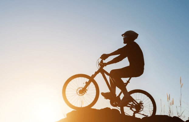 Electric mountain bike side view with rider on trail at sunset