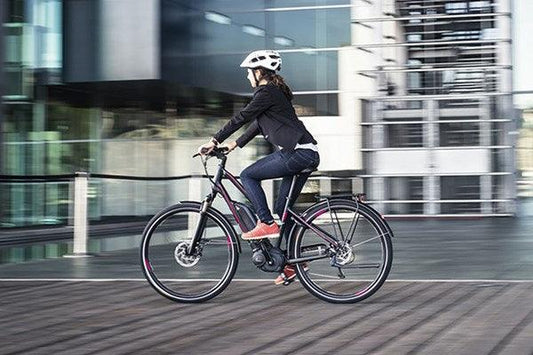 Electric commuter bike in matte black side view, ridden on city street by woman with helmet