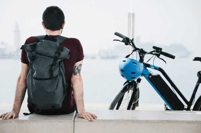Electric bike with blue frame and helmet, side view, near waterfront with person sitting