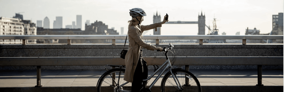 Step-thru electric bike silver side view, urban commuting, rider with helmet and phone on bridge