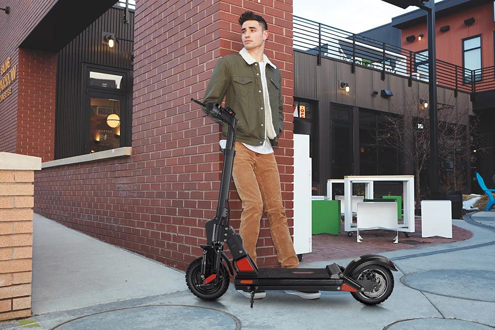 Man with black electric scooter parked on city sidewalk, side view